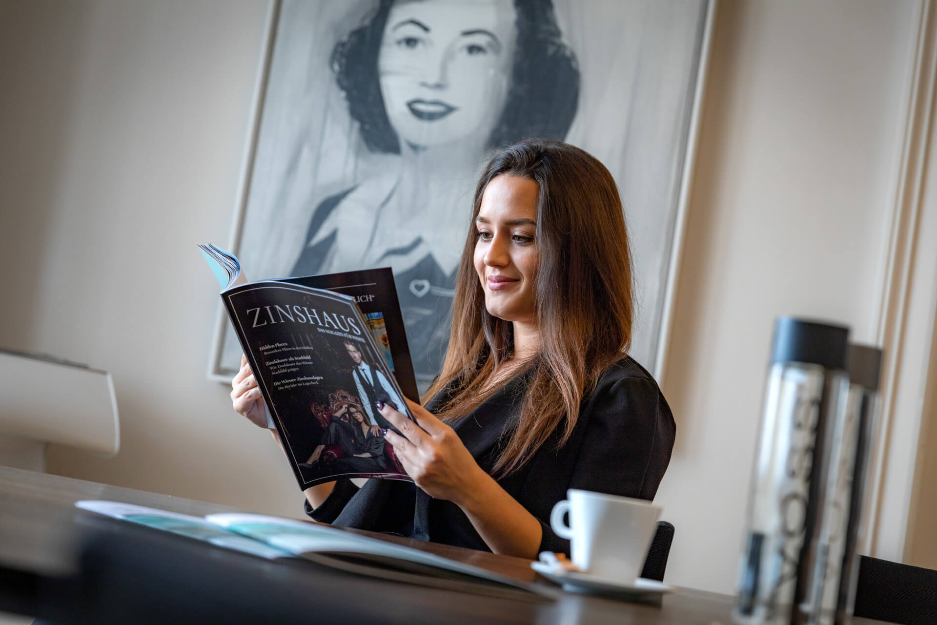 Eine Frau ließt gerade bei einem Kaffee das Zinhaus-Magazine
