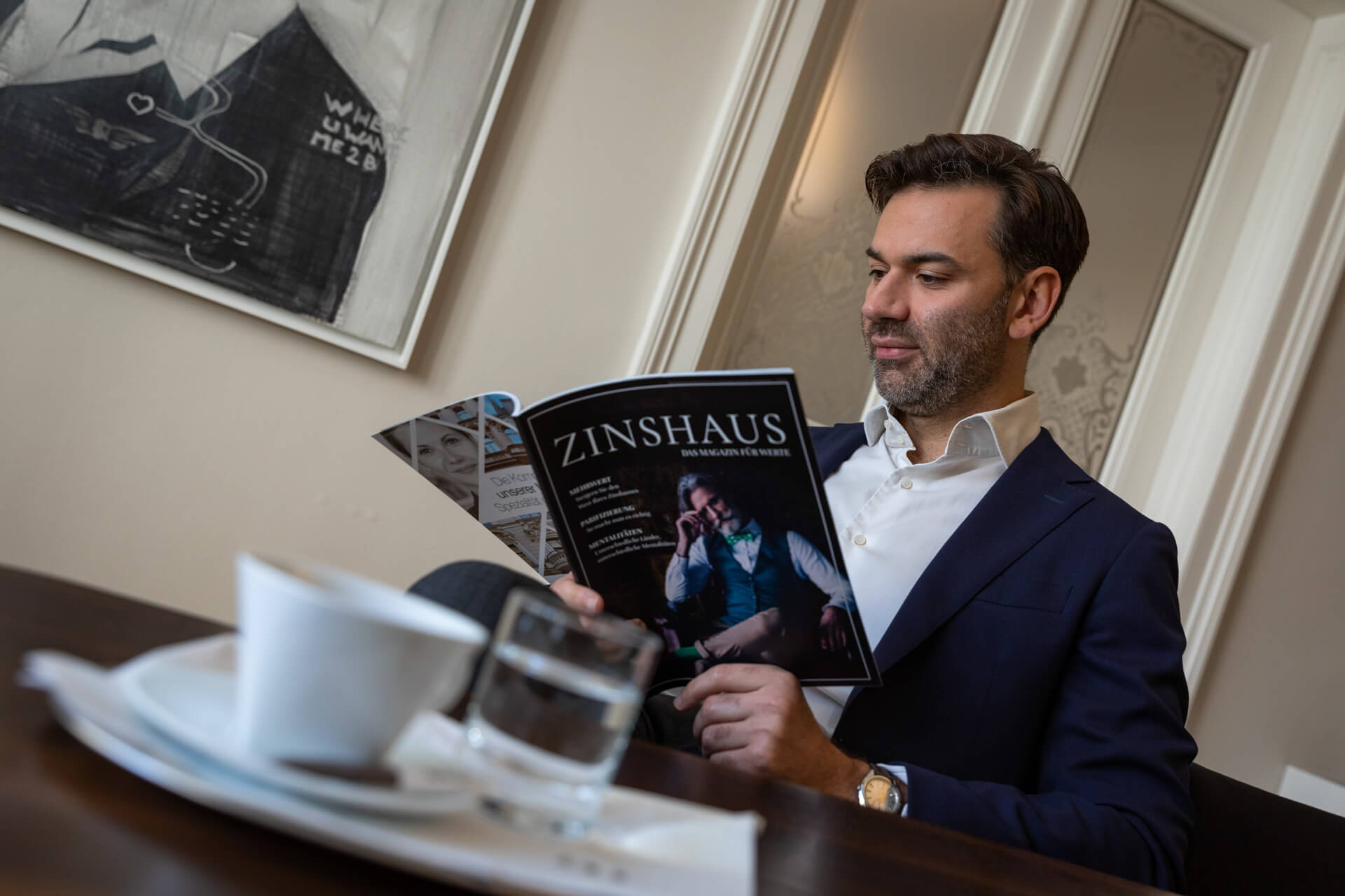 Ein Mann ließt gerade bei einem Kaffee das Zinhaus-Magazine