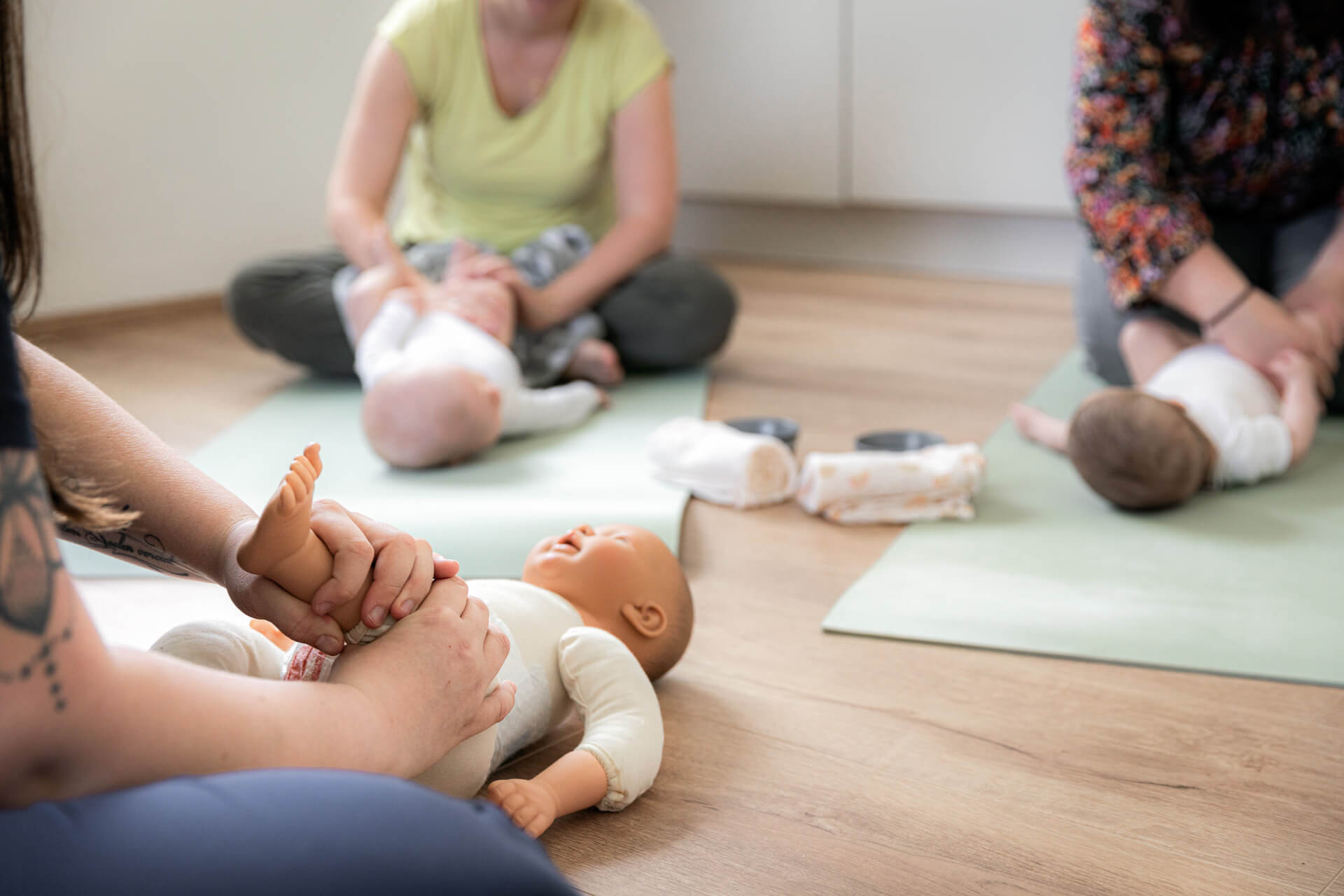die Babymassage wird anhand einer Puppe den Kursteilnehmern vorgeführt. zu sehen ist eine Puppe und zwei Babys.