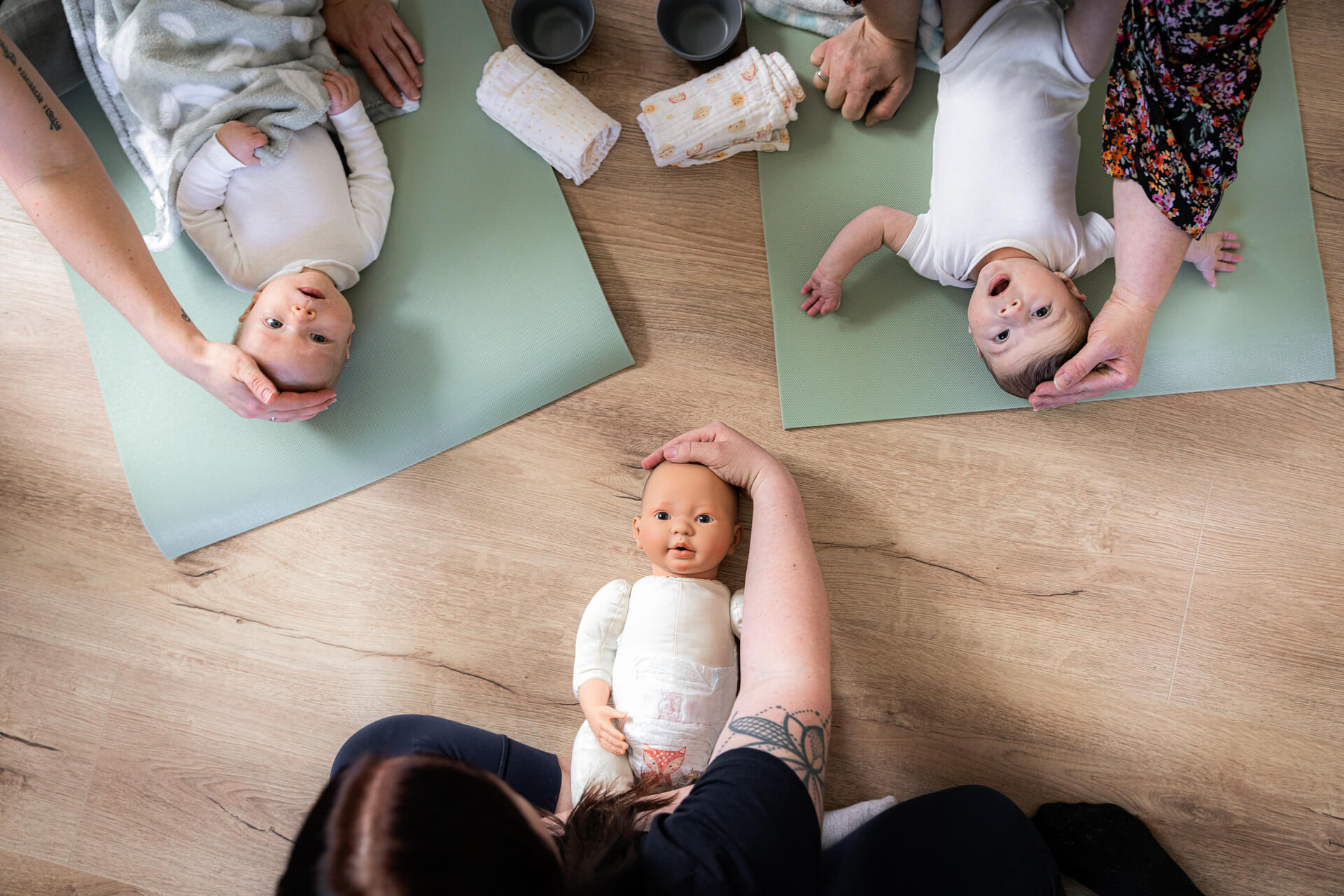 die Babymassage wird anhand einer Puppe den Kursteilnehmern vorgeführt. zu sehen ist eine Puppe und zwei Babys.