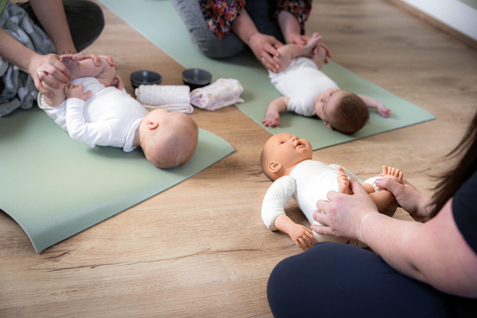 die Babymassage wird anhand einer Puppe den Kursteilnehmern vorgeführt. zu sehen ist eine Puppe und zwei Babys.