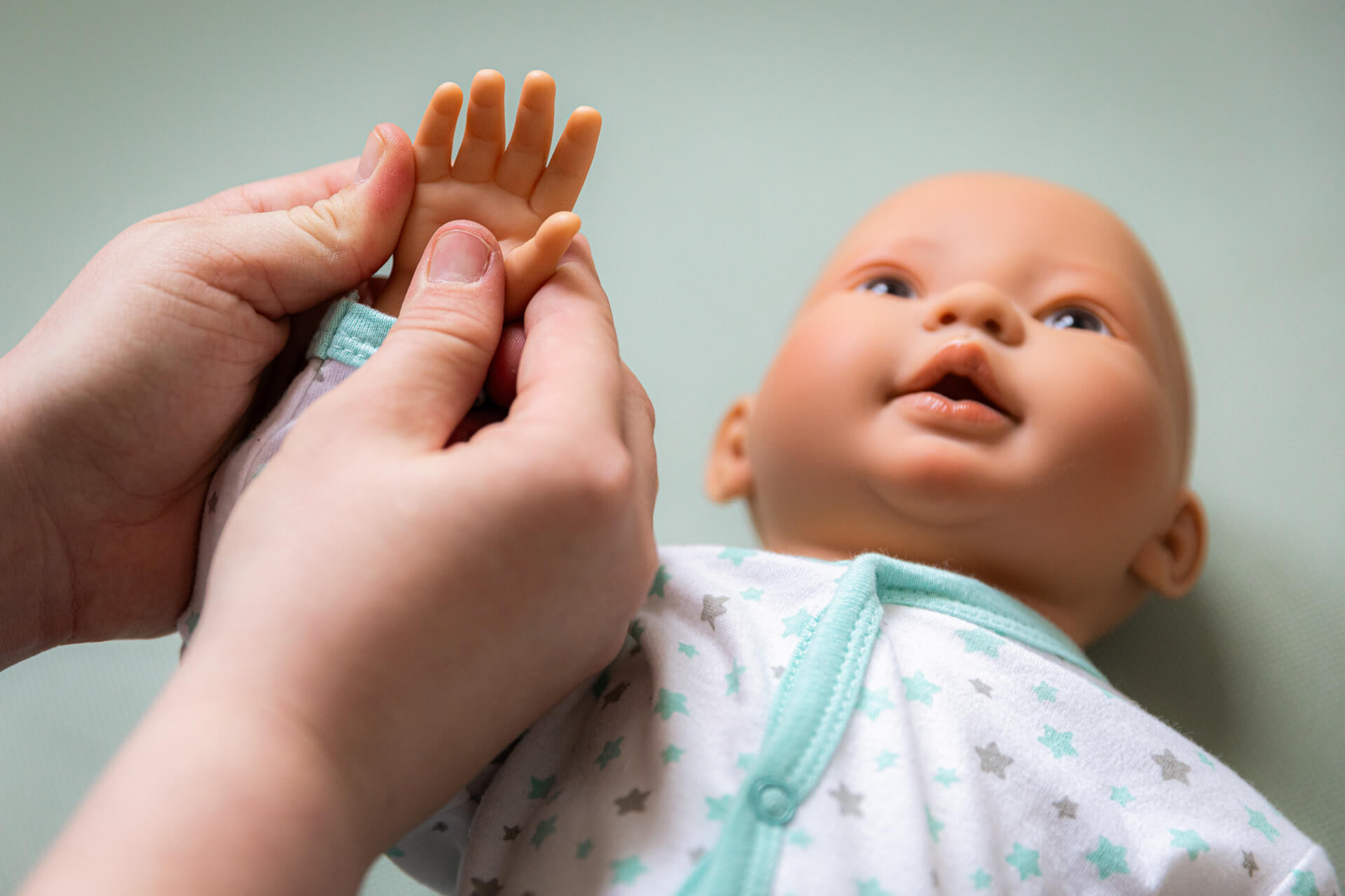 An einer Puppe wird eine Babymassage an der Hand vorgezeigt.